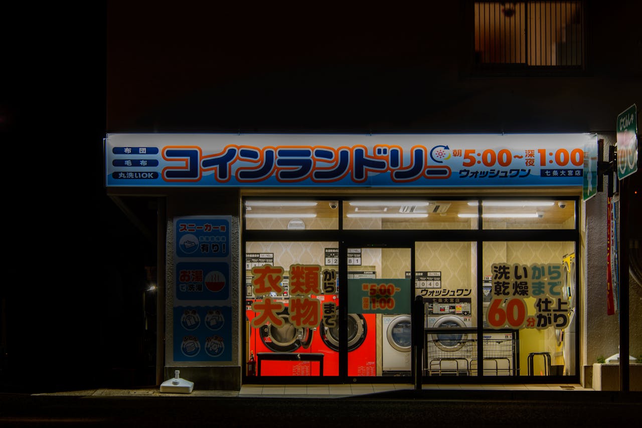 Vibrant nighttime view of a Kyoto coin laundry shop with illuminated signage and reflections.