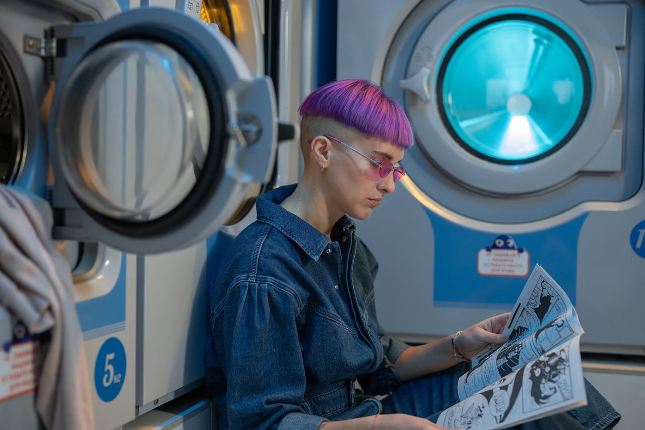 Young woman with dyed hair reading a comic book in a laundromat.